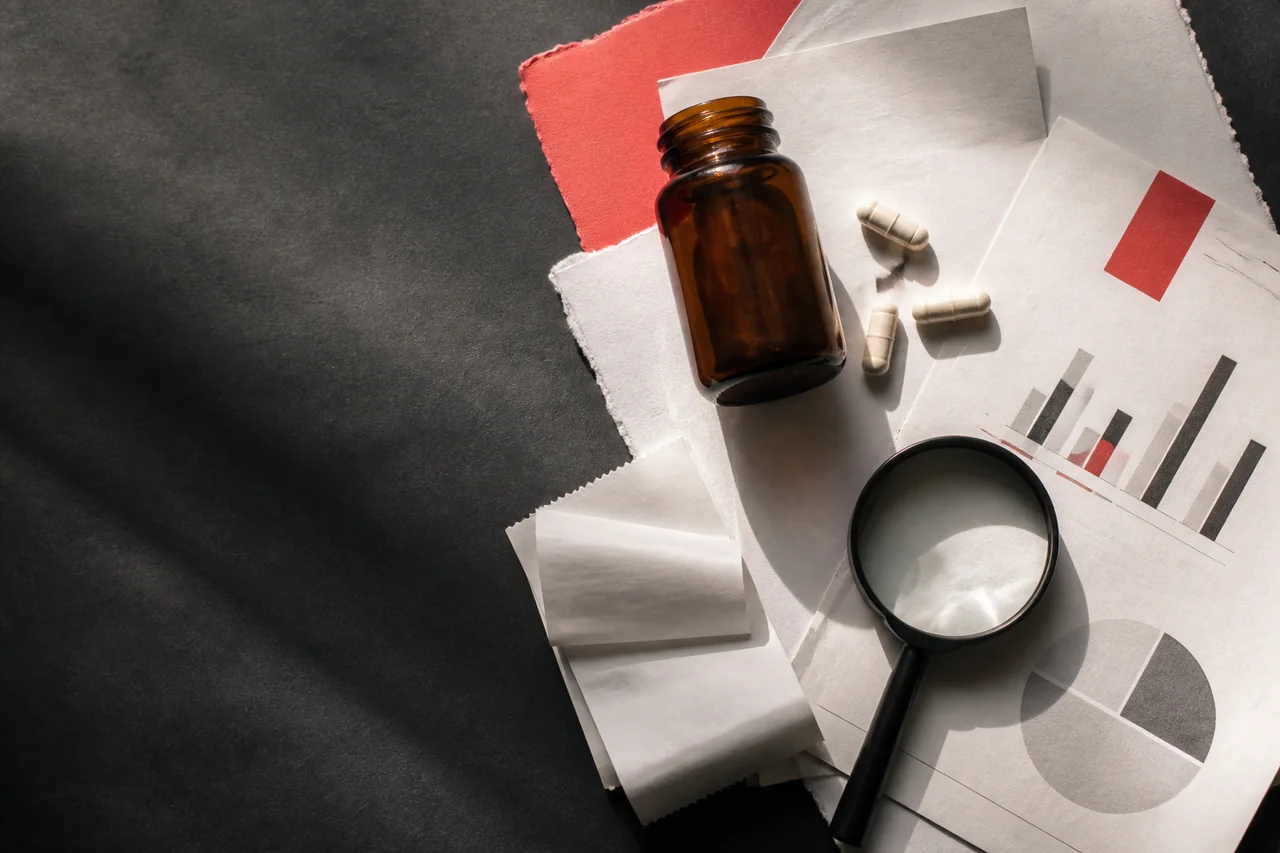 Amber supplement bottle, capsules, magnifying glass and evidence notes arranged on a dark desk